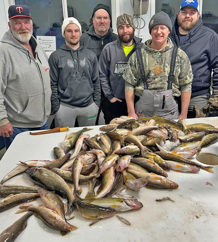 image of ice fishermen in front of walleyes stacked up on fish cleaning table